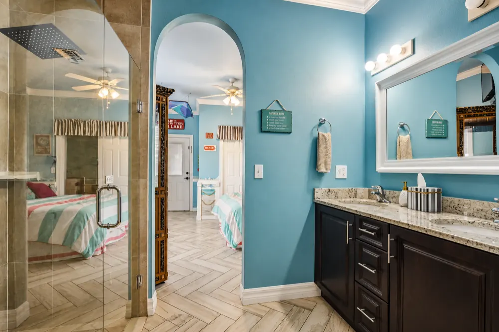 The Carnival suite bath: a glass walk-in shower with a rain head, the double granite vanity, and the arch back into the striped bedroom