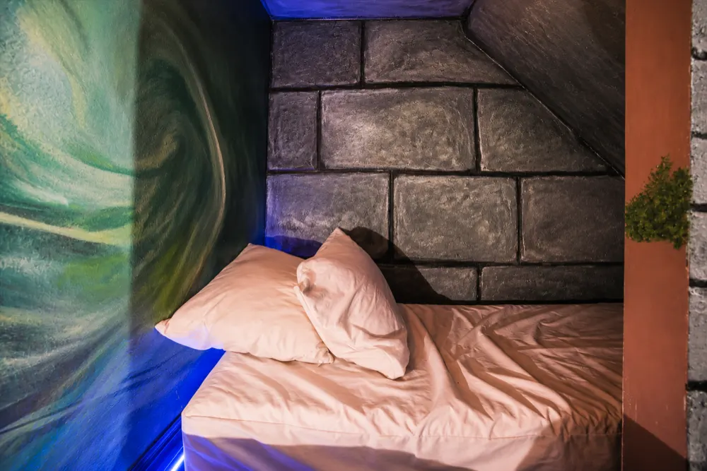 The bed at the end of the Dungeons and Dragons corridor: a single mattress and pillows under a painted stone wall, the dragon mural beside it