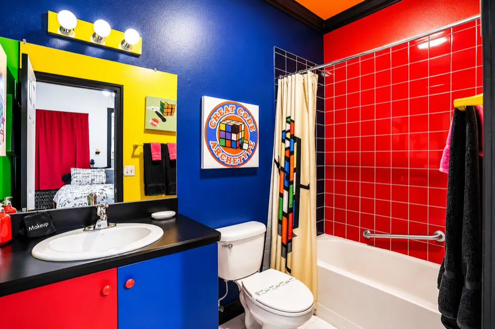 The Rubik bath: red tiled shower, blue and yellow walls, a red and blue vanity, a Cheat Code Archetype sign