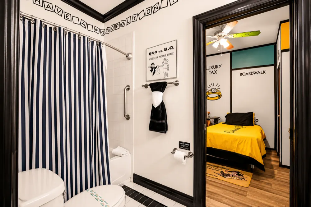 The Monopoly bath: a black and white striped shower curtain, a B and O versus B.O. hygiene sign, and the yellow Community Chest bed through the door