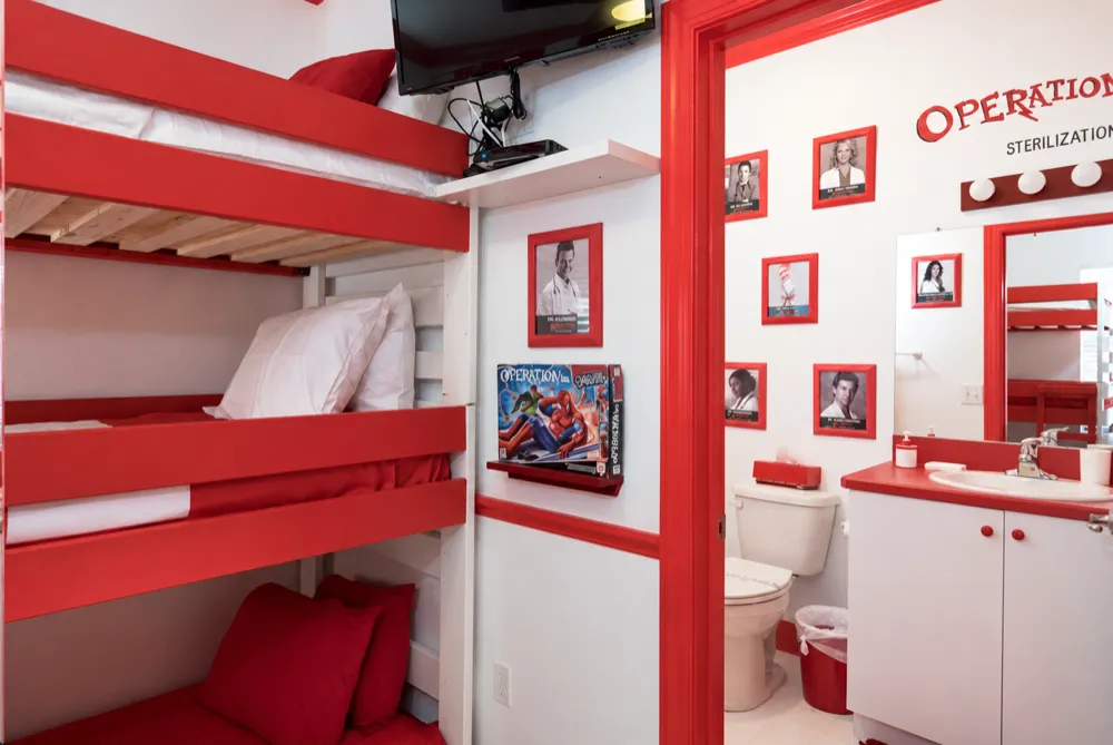 Triple bunk beds beside the open red door of the Sterilization Room bath, an Operation game box on the shelf