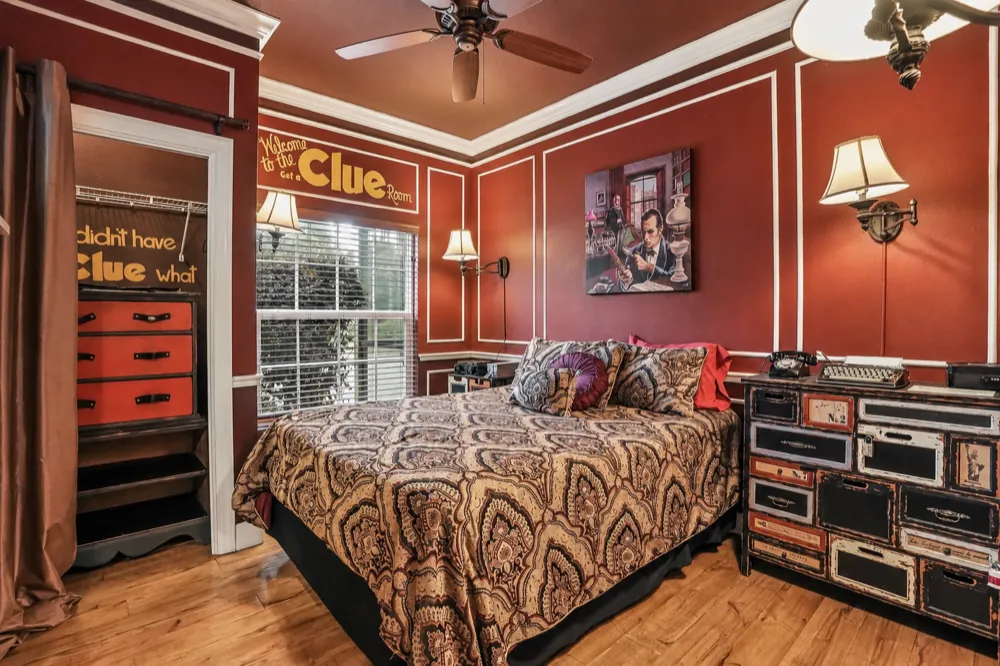 Get A Clue bedroom at Great Escape Lakeside: oxblood walls with white molding, a detective painting over the queen bed, a typewriter on a chest of numbered drawers