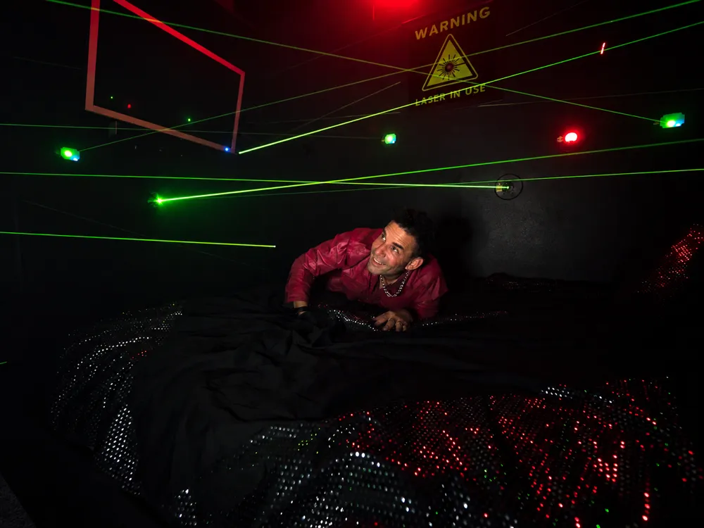 Laser Games room at Great Escape Lakeside: a guest on the king bed under green laser beams, the warning sign on the wall