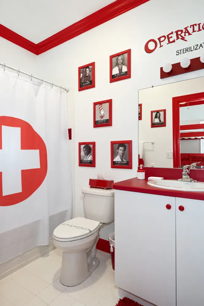 The Sterilization Room bath: red cross shower curtain, red-framed portraits of TV doctors, red and white vanity
