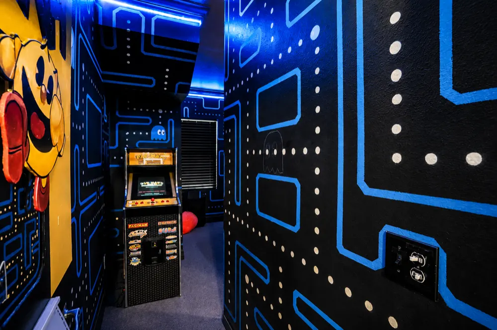 The hall into the Pac-Man bedroom: a coin-op arcade cabinet between maze walls lined with pellets, Pac-Man painted at the turn