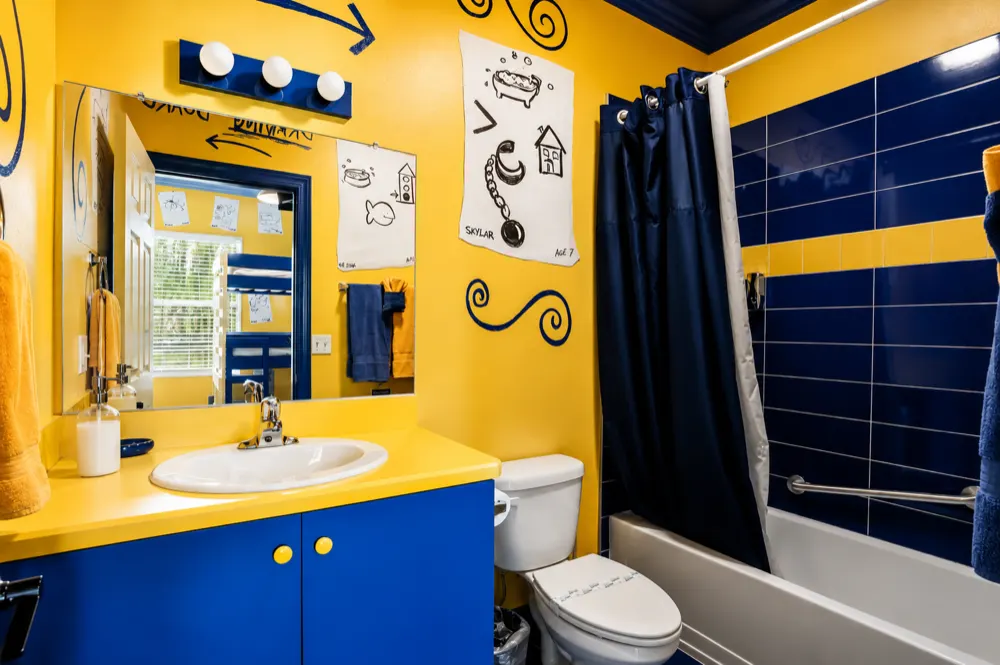 The Pictionary bath tub and shower: navy tiles with a yellow stripe, a navy curtain, a drawing of a bath and a fish signed Skylar, age 7