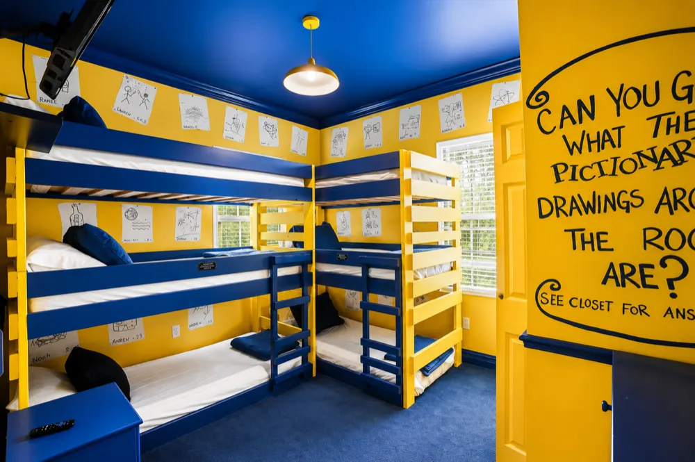 Pictionary bedroom: the wall TV, a hangman puzzle painted on the wall, and the Draw A Bath arrow pointing into the yellow and navy bathroom
