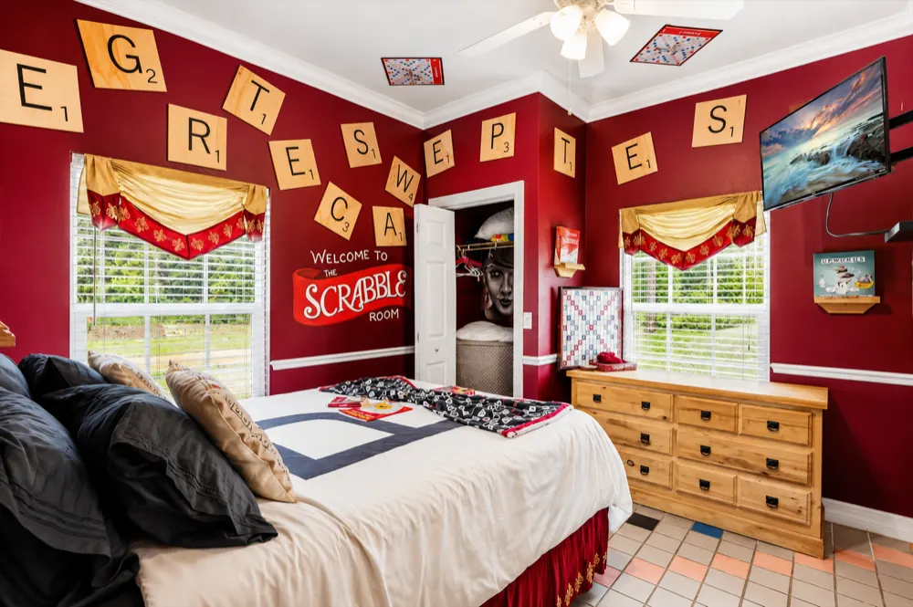 The Scrabble bedroom from the doorway: giant letter tiles on the red walls, the Welcome To The Scrabble Room sign, the queen bed, the windows and the dresser