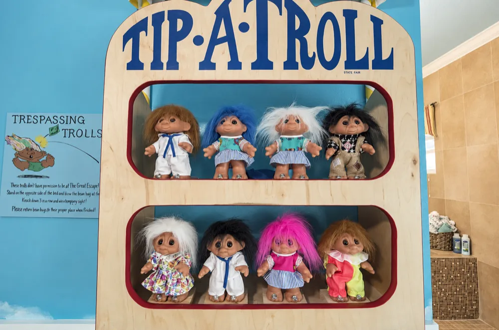 Tip-A-Troll booth with eight troll dolls on two shelves and the posted game rules beside it