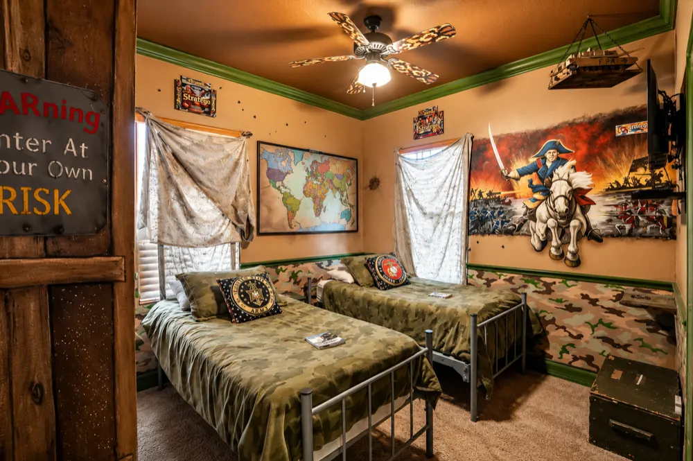 War Games bedroom at Great Escape Lakeside: two camo twin beds, a Risk world map, a Napoleon battle mural, a model tank hanging in the corner
